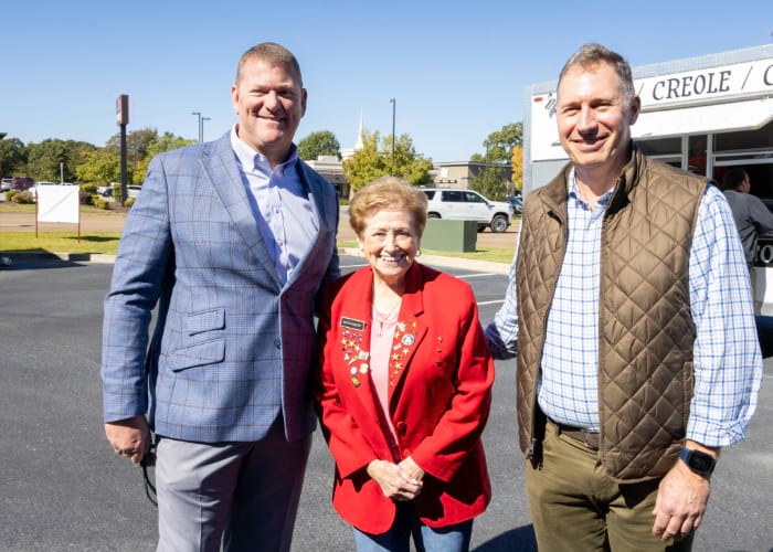 women wearing a red vest between two men smiling at the camera