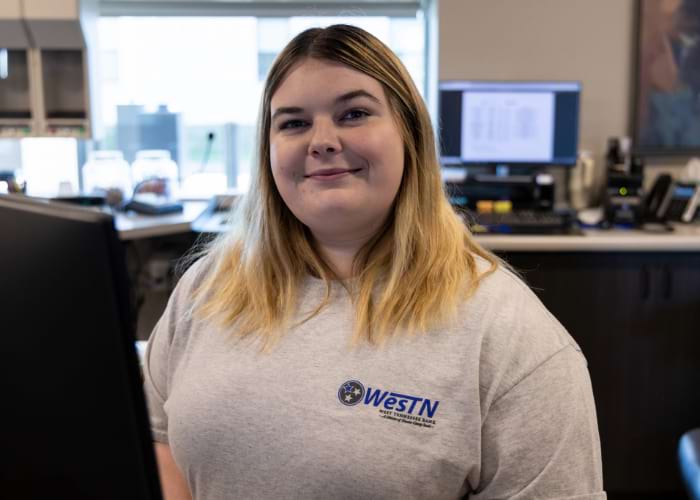 woman sitting at desk wearing a West Tennessee Bank shirt smiling at the camera