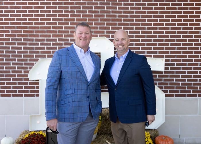 two men posing in front of 125 numbers