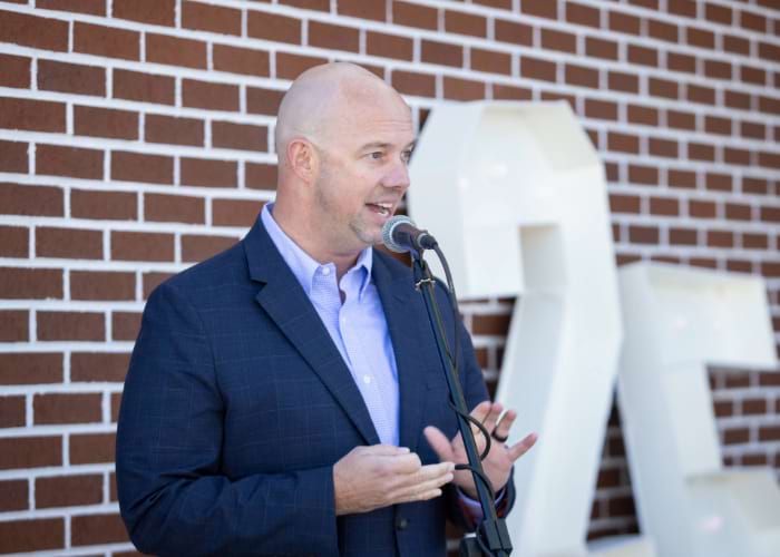Man dressed in a suit speaking into a mic