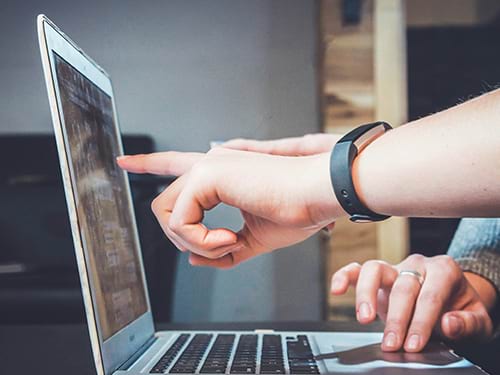 Someone pointing out something on a laptop screen while someone else types