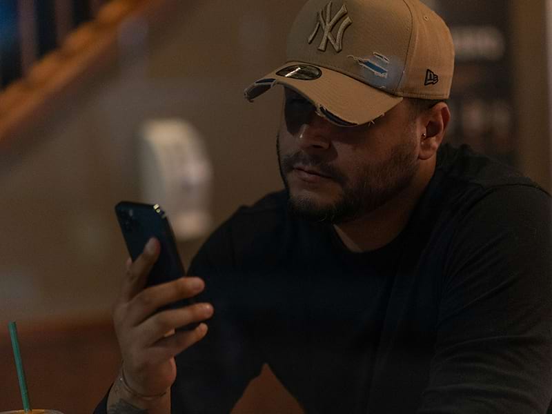 man with a hat in a dark room looking at phone