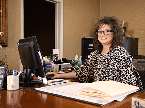 woman smiling at camera while sitting at her desk with her hand on her mouse