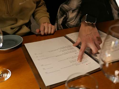 hand pointing out something on paper files on table with wine glasses