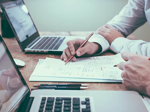 hands with pencils looking at paper between two laptops on table