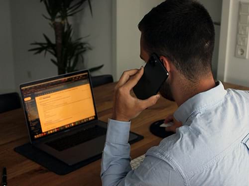 A man is on a phone call while looking up information on his laptop