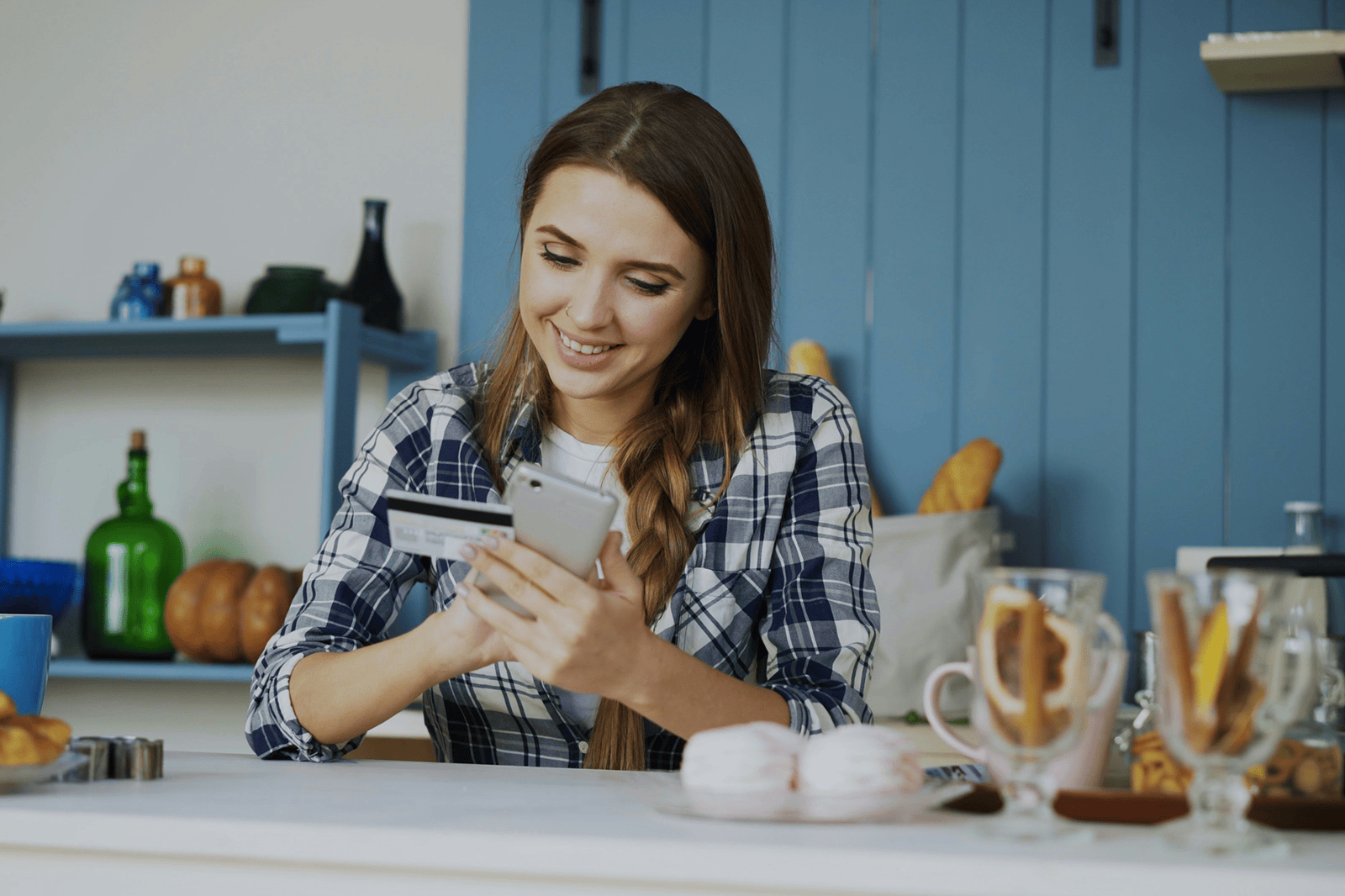 woman smiling at phone with card in hand while standing in kitchen
